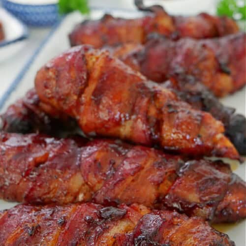 A white oblong plate with blue trim filled with half a dozen bacon wrapped smoked chicken strips.