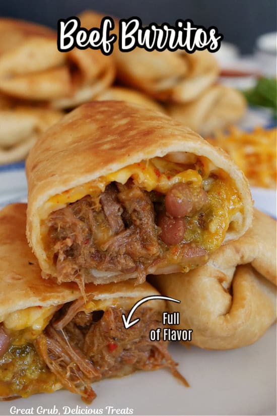 Two fried shredded beef burritos on a white plate with one of them cut in half and one piece placed on top of the others.