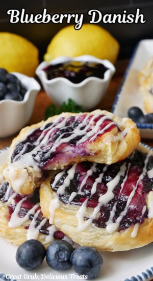 Three blueberry danishes on a white round plate with blue trim with a bite taken out of one of them.