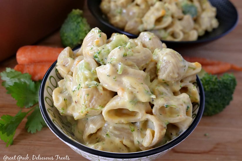Broccoli Cheddar Mac and Cheese is a creamy and delicious take on classic mac and cheese that is loaded with cooked broccoli and shredded carrots. A close up photo of broccoli mac and cheese in a bowl with a black trim, with broccoli florets and carrots in the background.