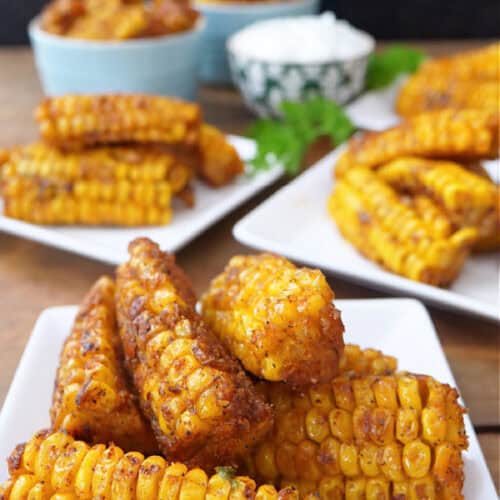 Three white square plates with deep fried corn ribs on them.