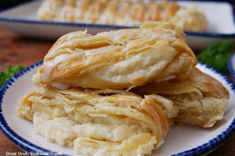 A few slices of cheese danish on a round white plate with blue trim with another pastry braid in the background.