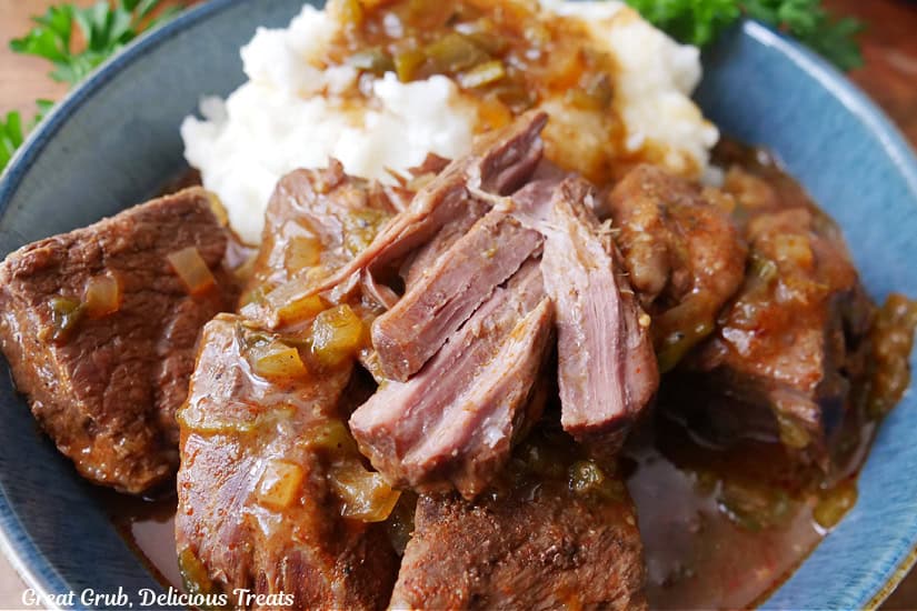 A serving of beef roast in a blue bowl with a scoop of mashed potatoes and gravy.