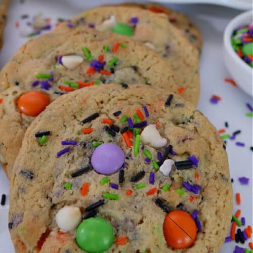 A few Halloween cookies on a white surface with candy sprinkles placed around the cookies.