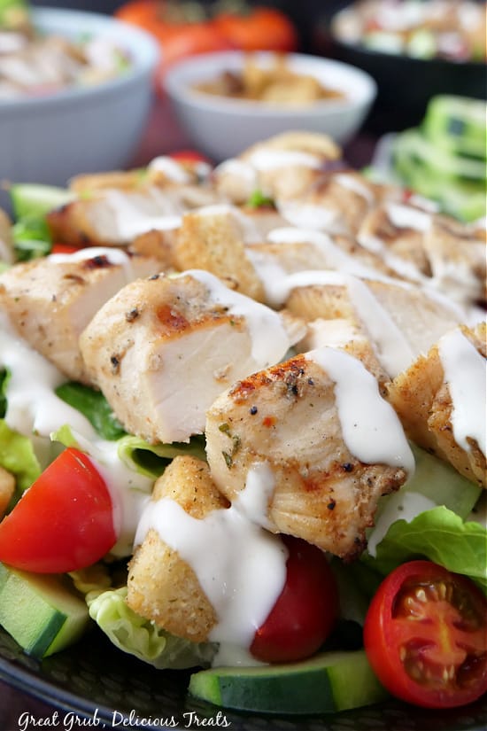 Grilled Chicken Salad is loaded with tender and perfectly cooked chicken, romaine lettuce, cherry tomatoes, cucumbers, ranch dressing, and croutons. A close up pic of diced chicken on a bed of lettuce with ranch dressing drizzled on top.