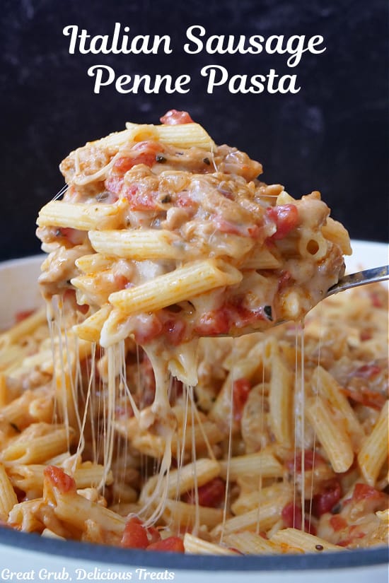 A serving spoon scooping out a big spoonful of cheesy pasta with sausage.