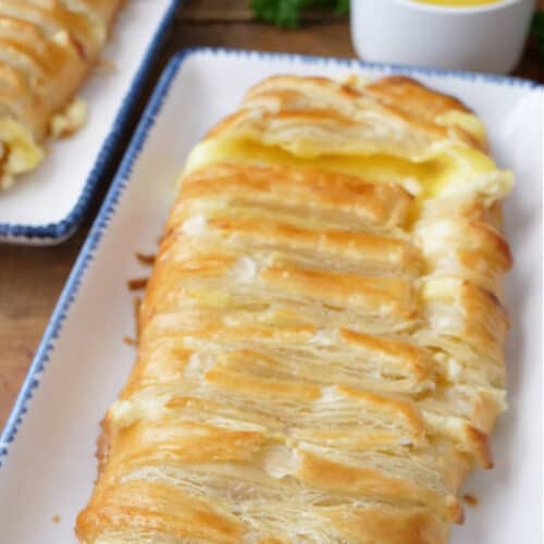 Two lemon puff pastries on two rectangle white plates with blue trim with two small white bowls filled with lemon pie filling and cream cheese mixture.