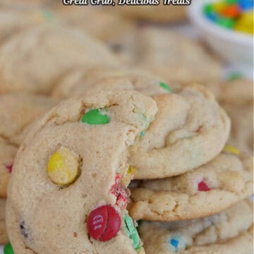 A white surface with mini peanut butter cookies placed all over the surface with a few stacks of cookies and one with a bite taken out of it.