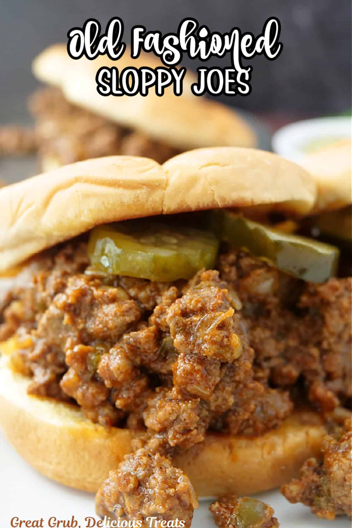 A sloppy joe on a counter showing the meat and pickles in a toasted bun with the title of the recipe at the top.