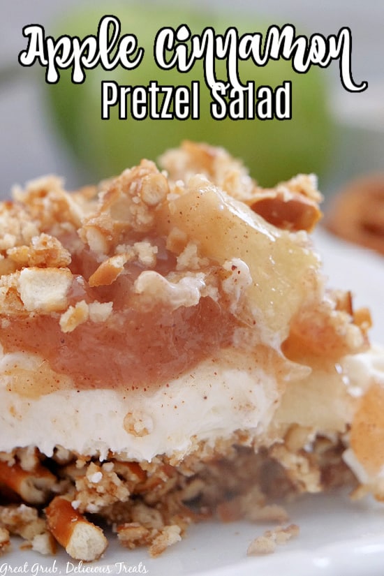 A white plate with a piece of apple salad, with crushed pretzel crust, a whipped cream filling, all topped with a cinnamon apple topping.
