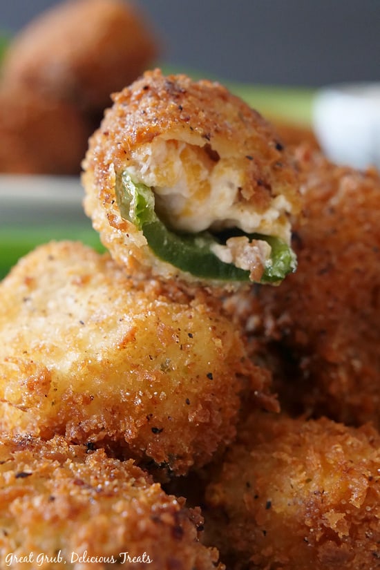 Stuffed Jalapeno Poppers are crispy, crunchy and filled with a deliciously seasoned cream cheese filling consisting of crispy bacon, shredded cheese and green onions. Another close up view of a stuffed jalapeno popper that has a bite taken out sitting on a stack or more poppers.