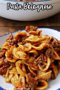 A white bowl with blue trim filled with a serving of pasta bolognese.