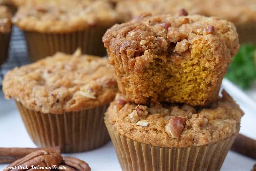 A white surface with pumpkin muffins on it with a bite taken out of one of the muffins.
