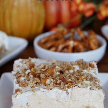 A square white plate with a serving of pumpkin pretzel dessert on it with fall foliage in the background.