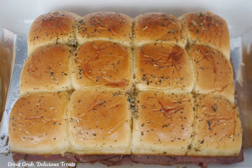 A white baking dish with 12 sliders in it.