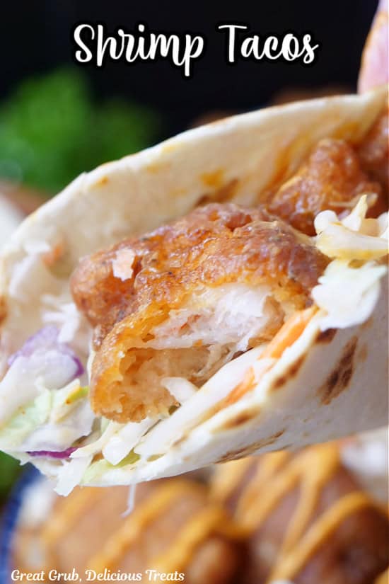 A shrimp taco with a bite taken out of it.