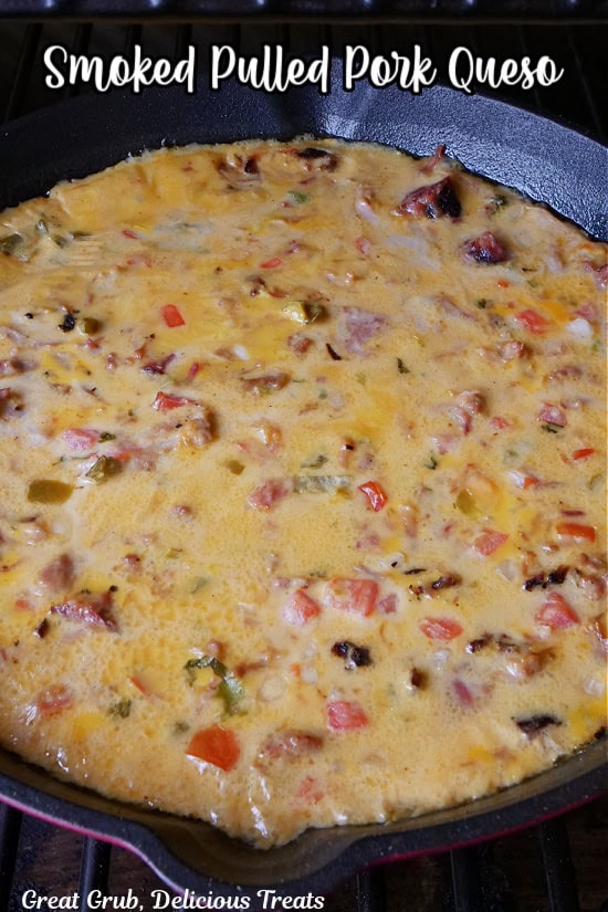 A red and black cast iron pan with smoked pulled pork queso in it.