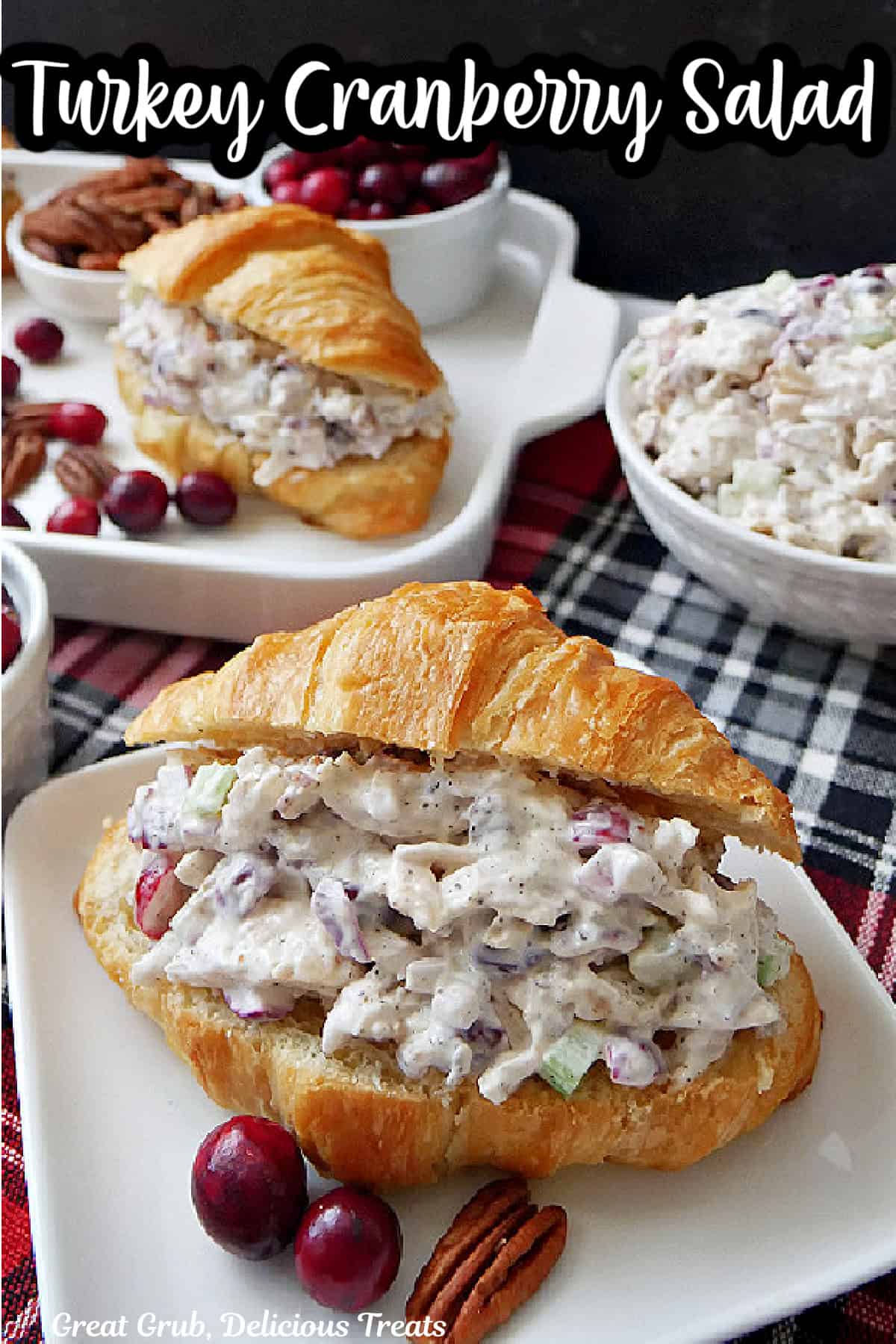 A red and black plaid surface with white plates with croissants filled with turkey cranberry salad.