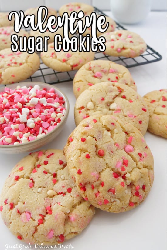 A white surface with sugar cookies on it and more cookies on a wire rack.